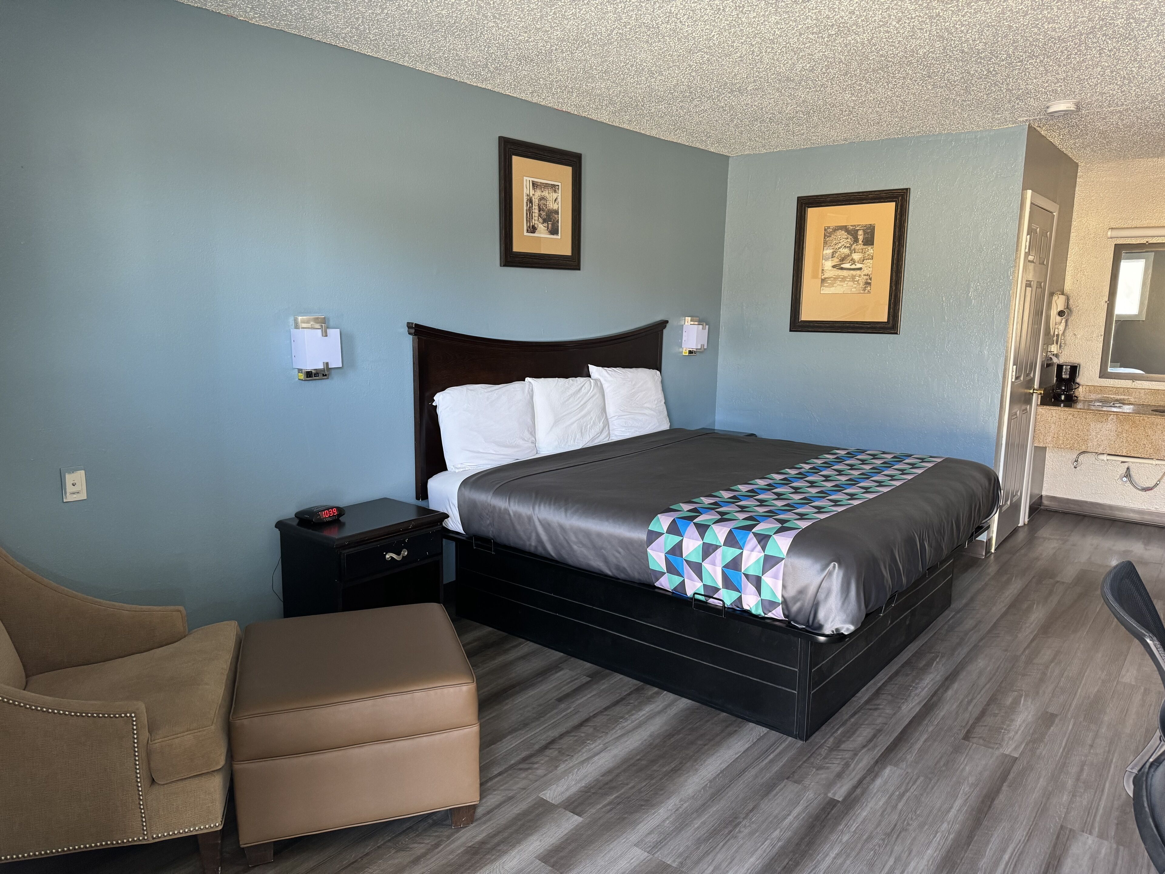 A hotel room with a bed, a nightstand, a chair, and a bathroom visible through an open door.