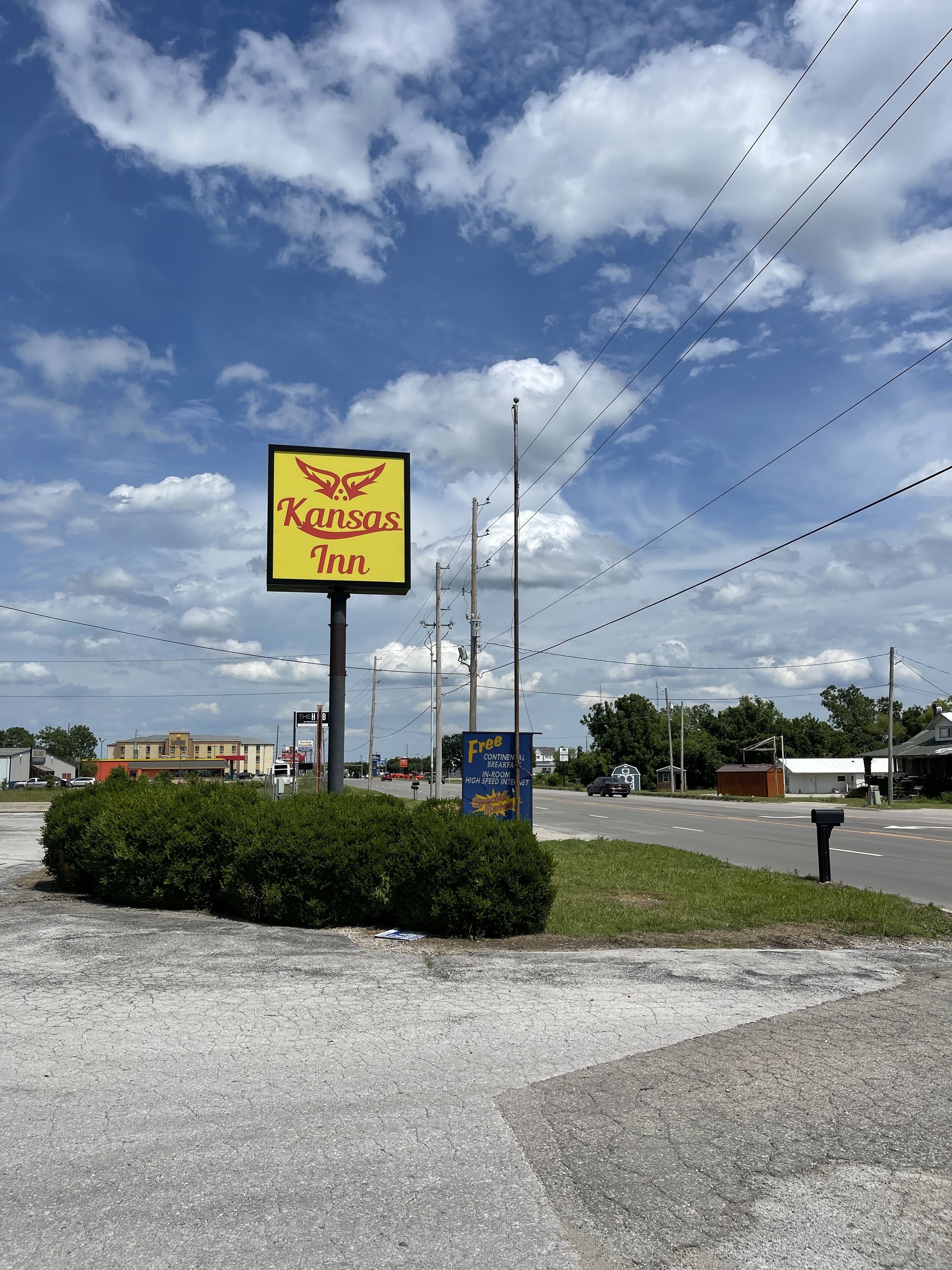 Señal de Kansas Inn con una vista despejada del entorno, incluyendo una carretera, líneas eléctricas y un edificio al fondo.
