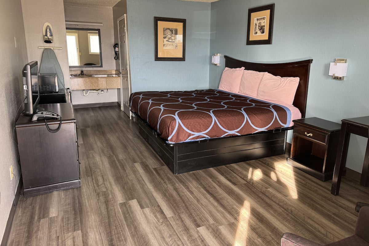 A hotel room with a bed, a desk, a chair, a television, and a bathroom visible through an open door.
