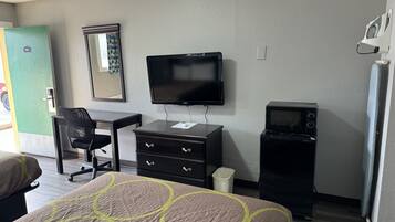 Een hotelkamer met een bed, bureau, stoel, televisie, magnetron en prullenbak.