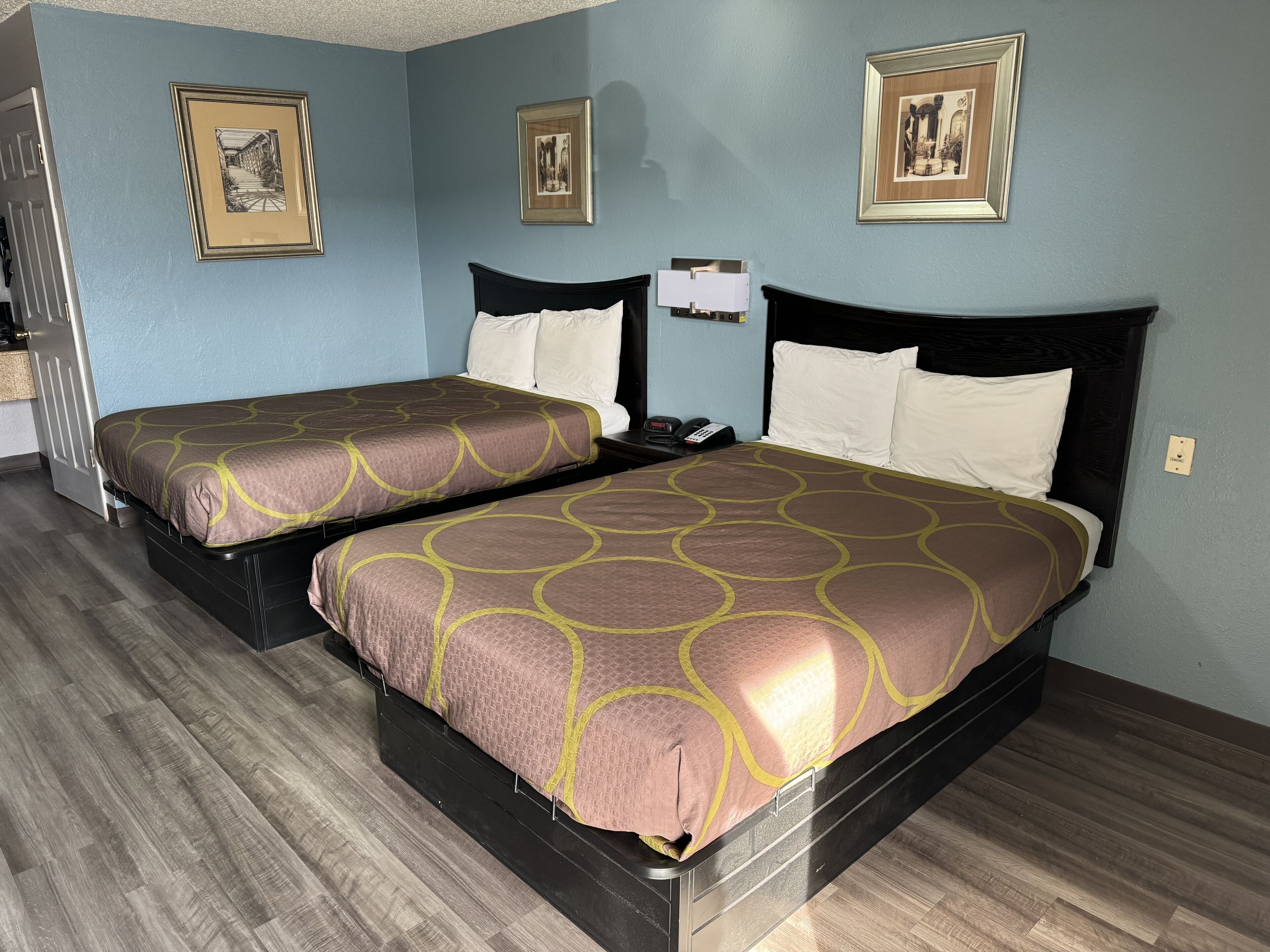 Quarto de hotel com duas camas, cada uma com colcha estampada, mesa de cabeceira com abajur e quadros nas paredes.