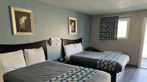 Habitación de hotel con dos camas, una mesita de noche, una lámpara de pared y una ventana con cortinas estampadas.