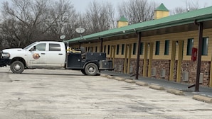 Una camioneta blanca estacionada en un motel con techo verde y paredes de ladrillo.
