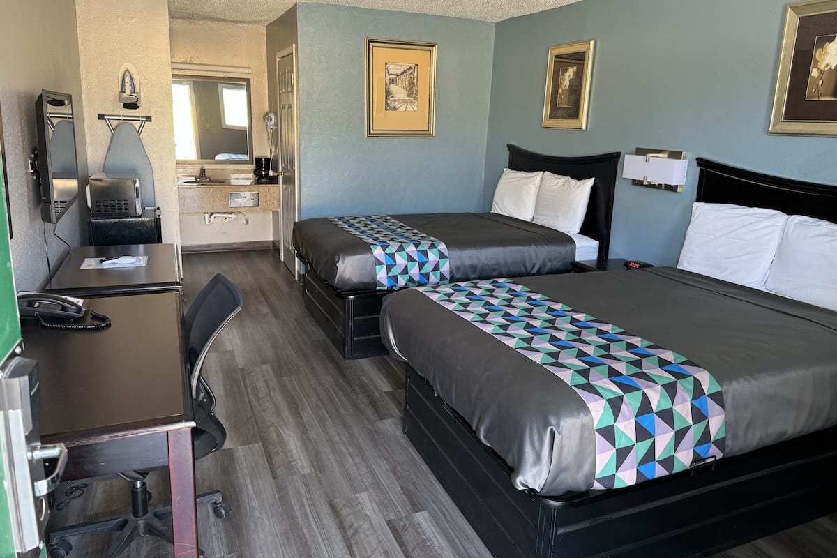 A hotel room with two beds, a desk with a telephone, a chair, a coffee maker, and framed pictures on the wall.