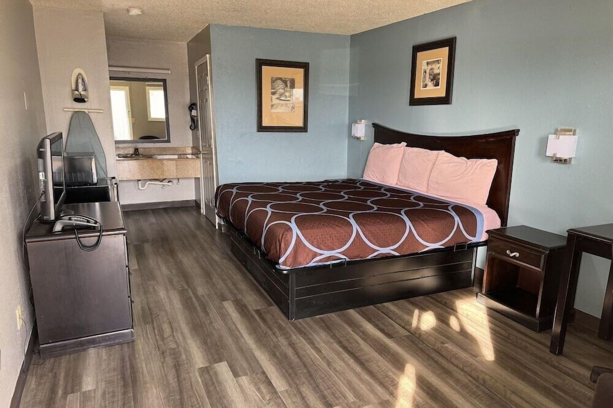 A hotel room with a bed, a desk, a dresser, and a mirror.