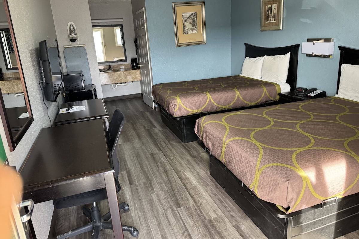 A hotel room with two beds, a desk, a chair, a desk lamp, a telephone, and a mirror.