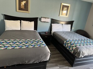 A double bed with a geometric patterned bedspread, a bedside table with a clock, and a framed picture on the wall.