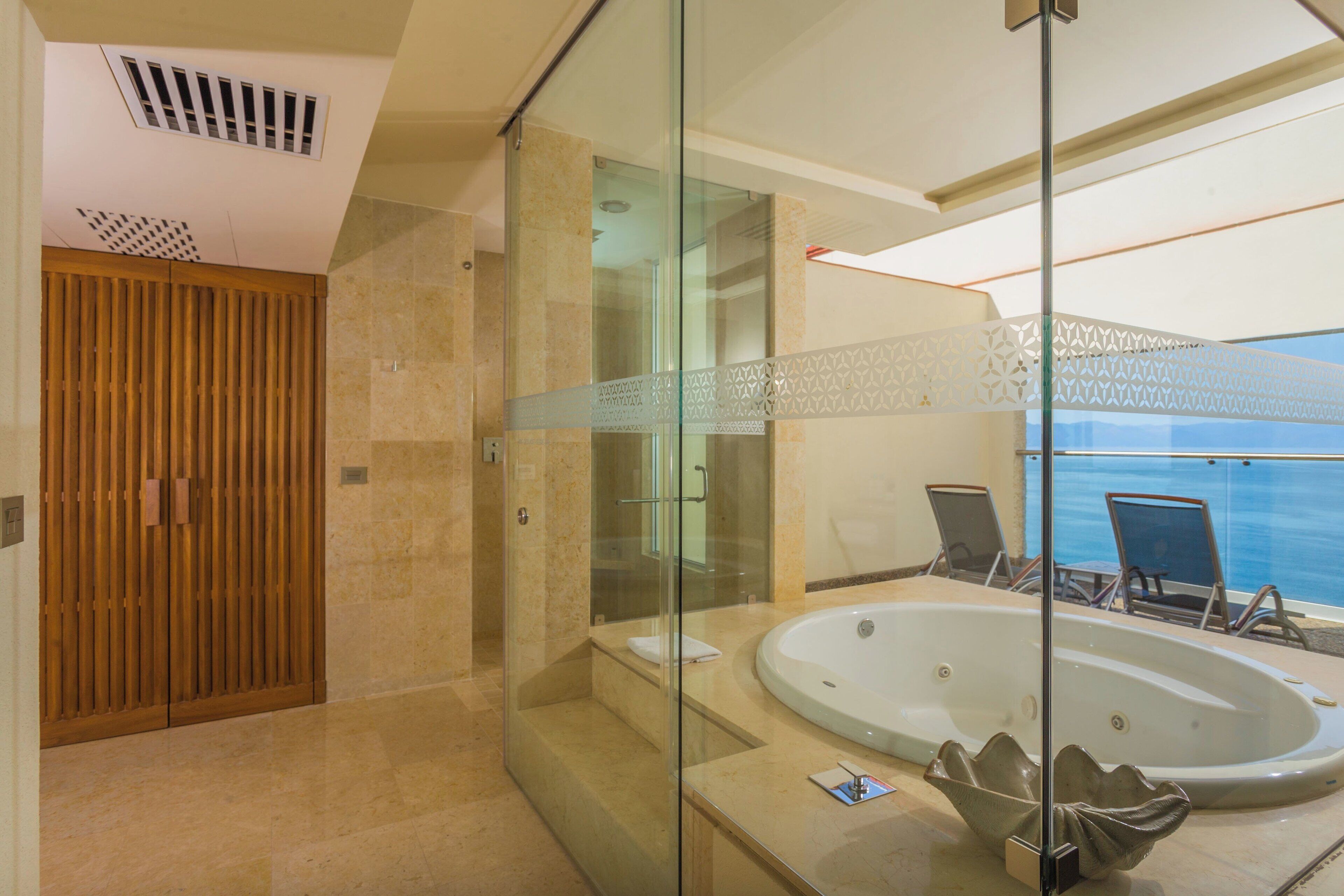 Un baño moderno con ducha de vidrio, una bañera grande y vistas al mar.