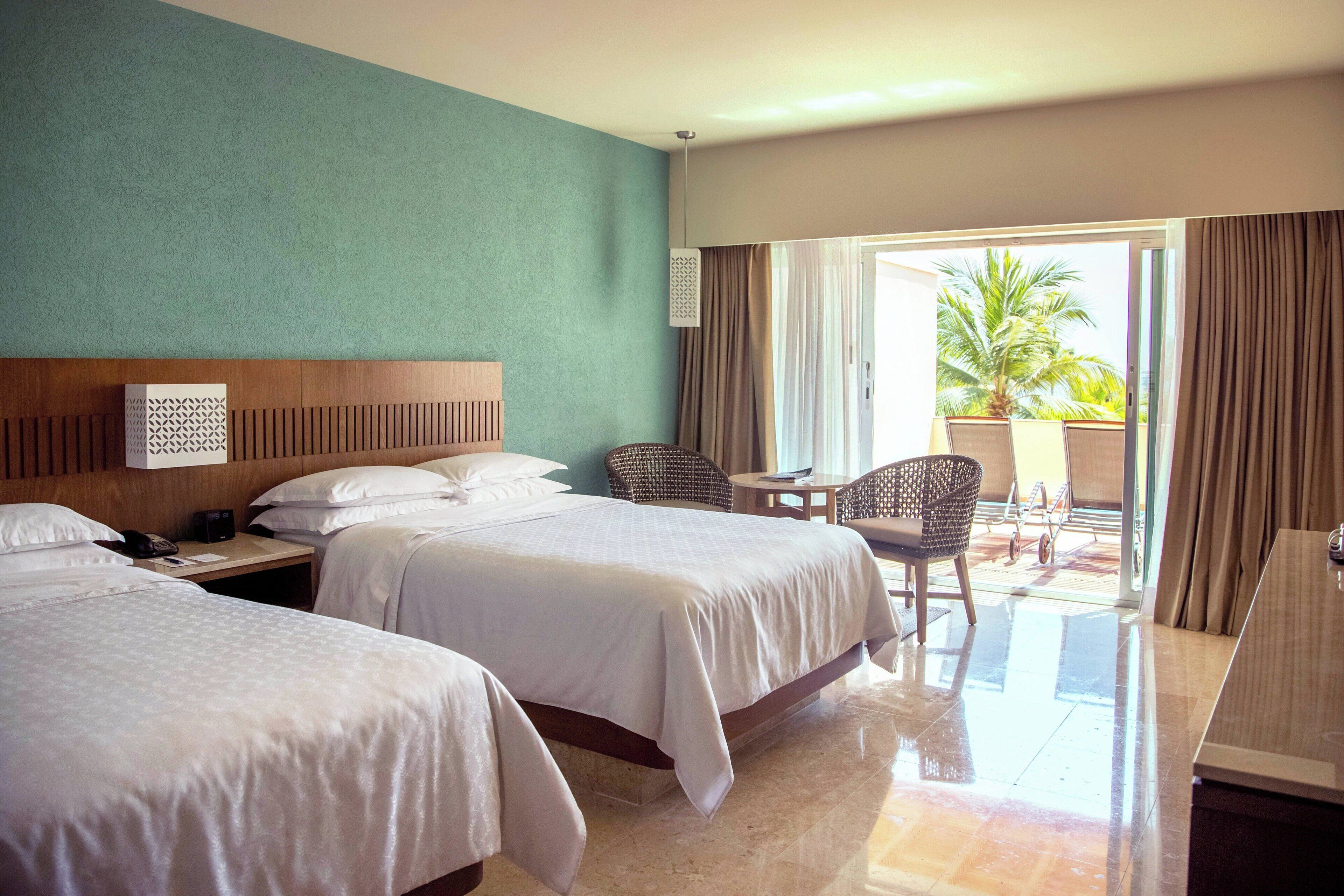 Habitación de hotel con dos camas, cabecero de madera, una mesita pequeña y una silla.