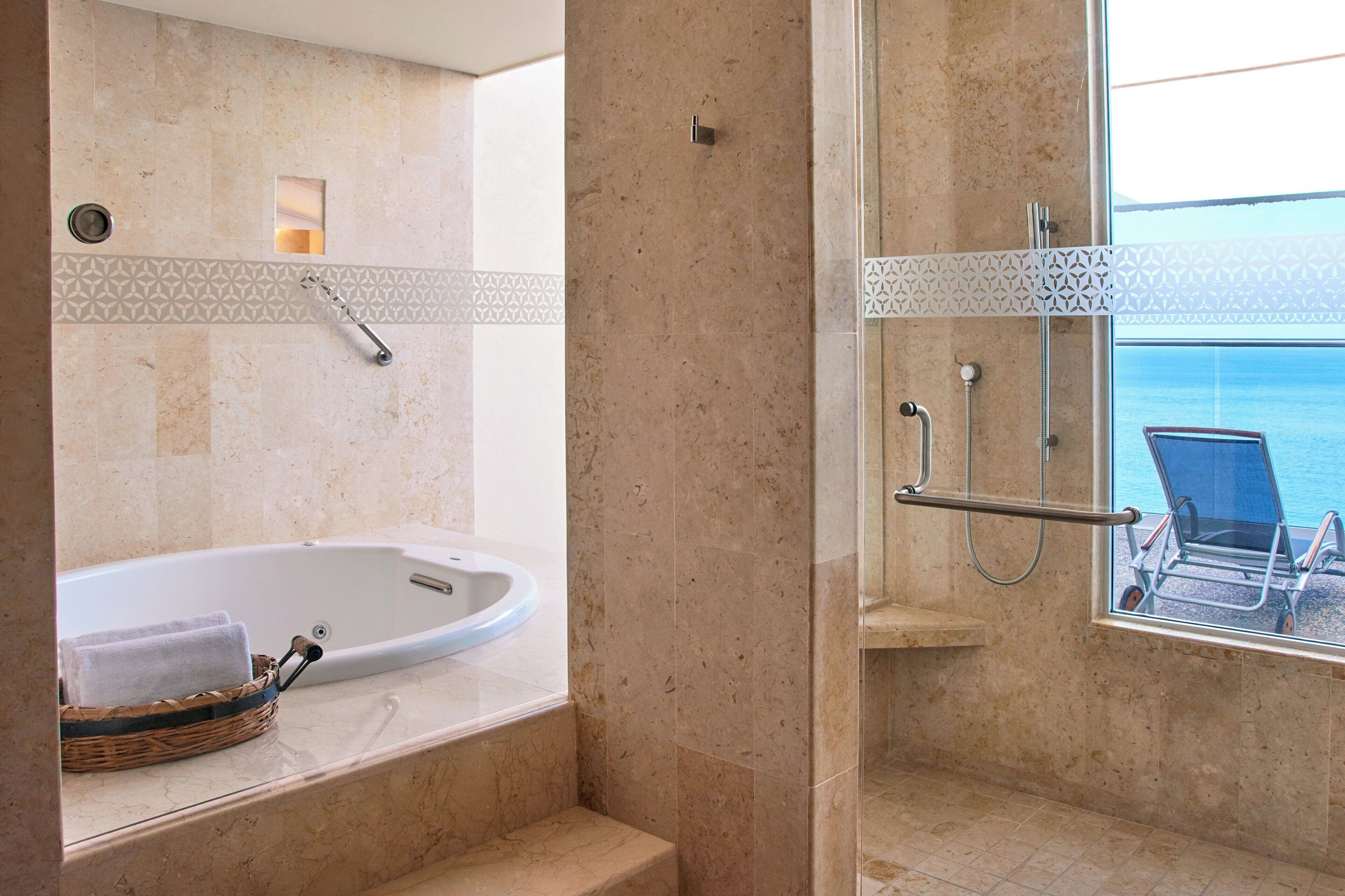 Un baño con bañera, ducha y ventana con vista al mar.