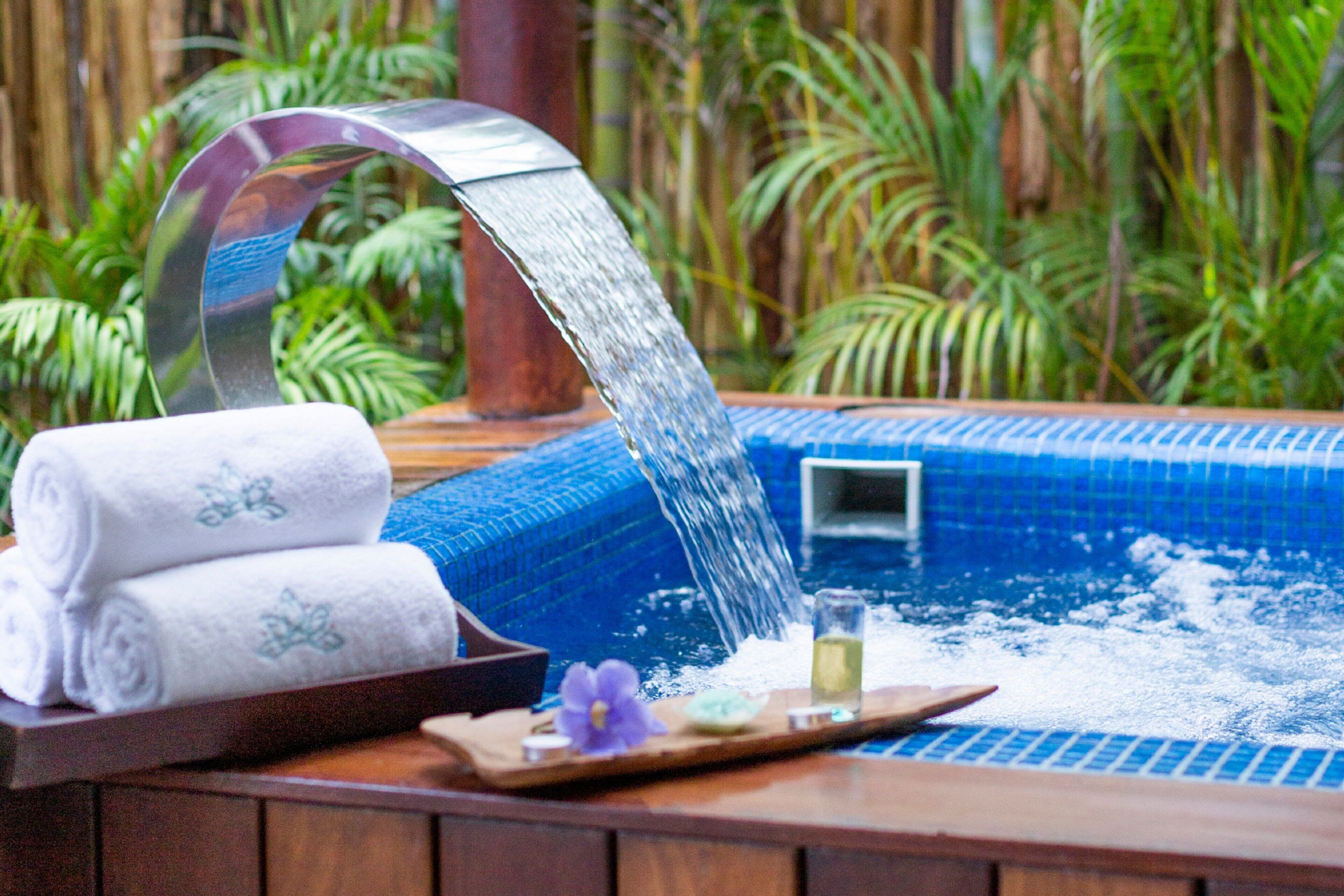 A hot tub with a waterfall feature, surrounded by lush greenery.