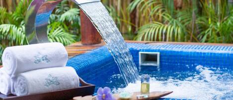 A hot tub with a waterfall feature, surrounded by lush greenery.