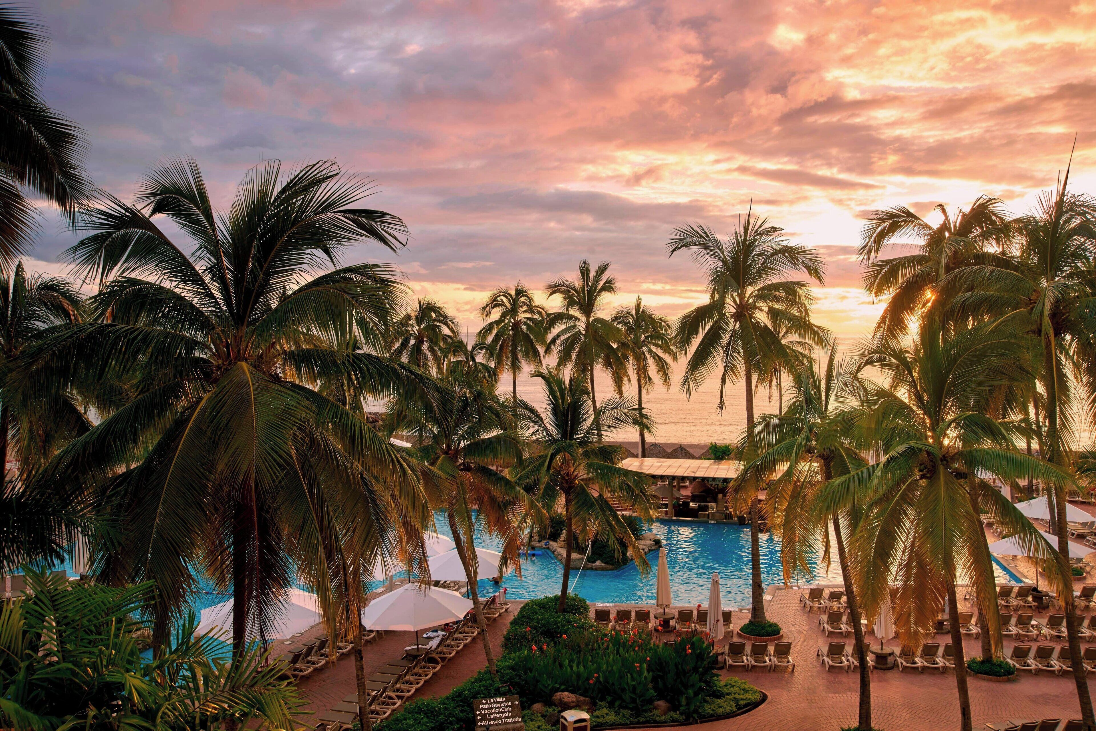Ein Poolbereich eines Resorts mit Palmen, Liegestühlen und Sonnenschirmen.