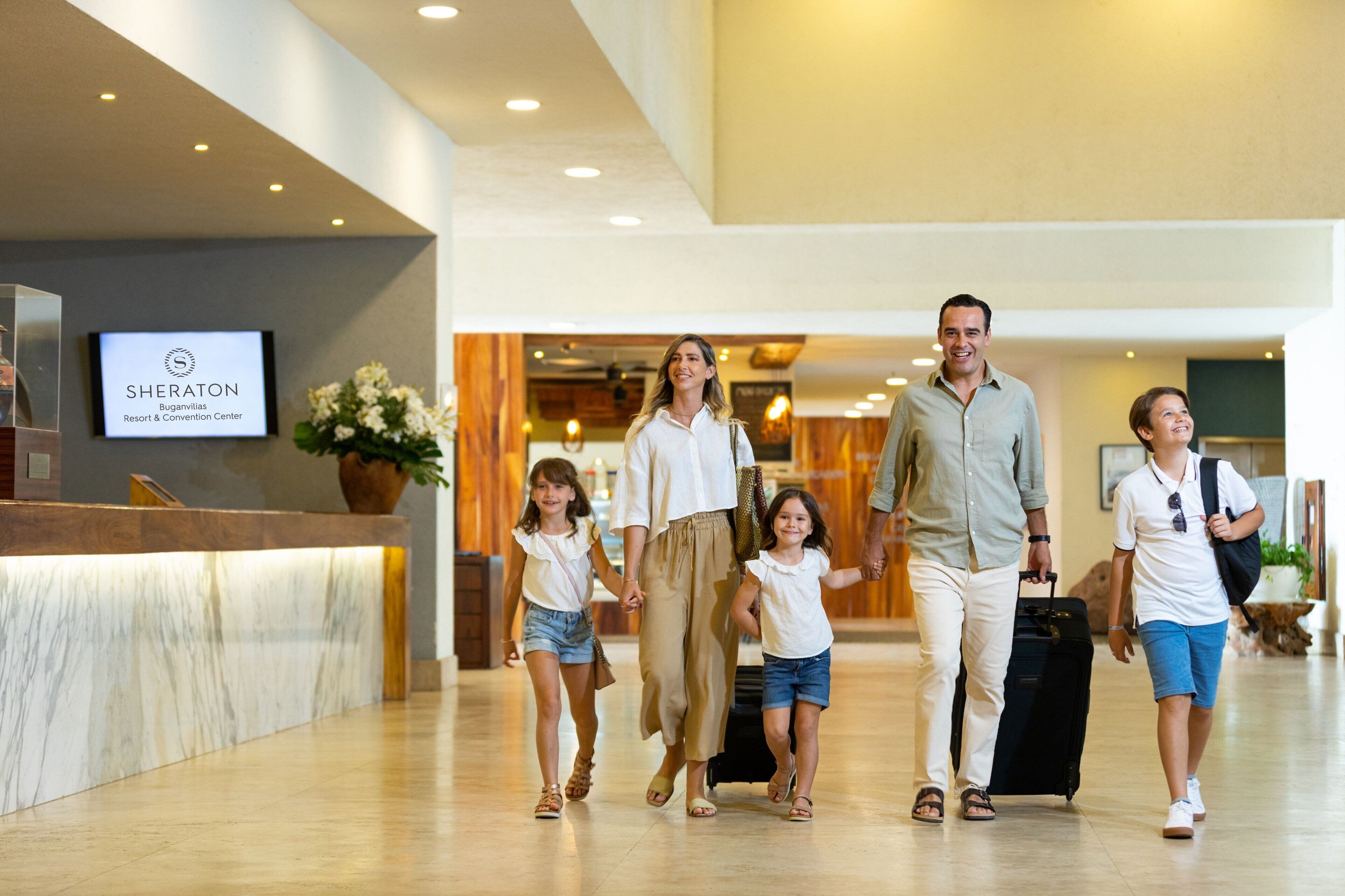 A family walking through a hotel lobby with a reception desk and a sign for Sheraton Resort & Convention Center.