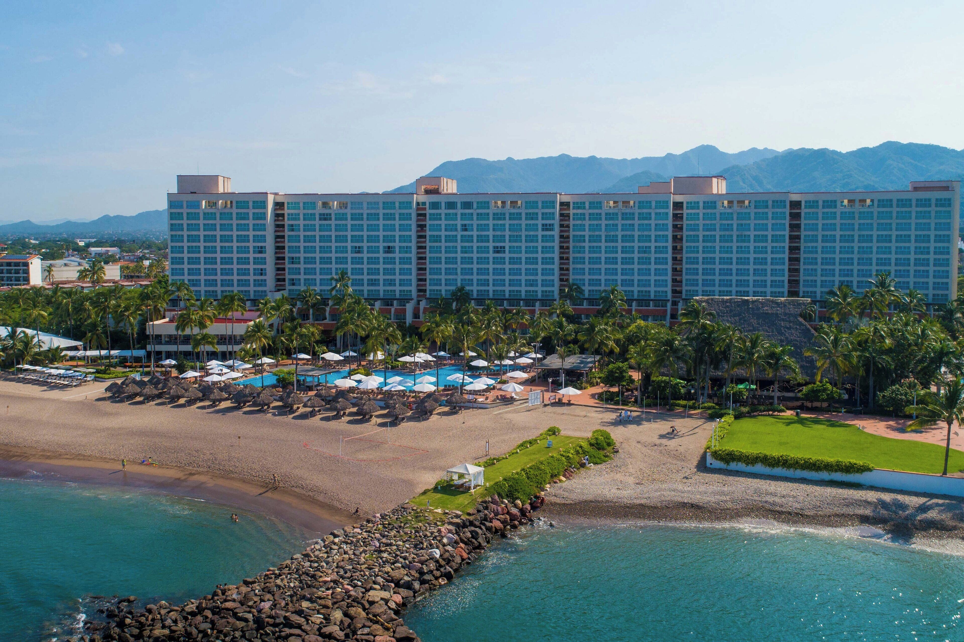 A large hotel with a beach and pool area, surrounded by mountains.