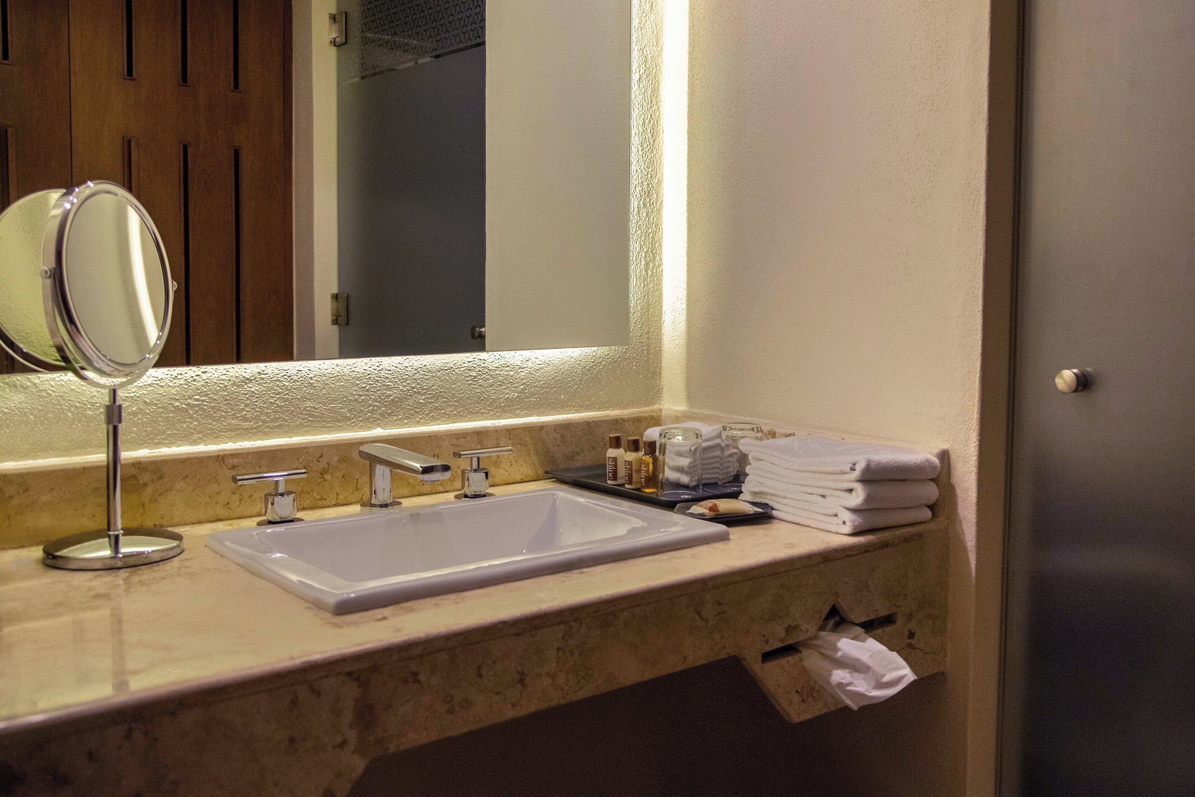 Un baño con lavamanos, espejo y artículos de aseo.