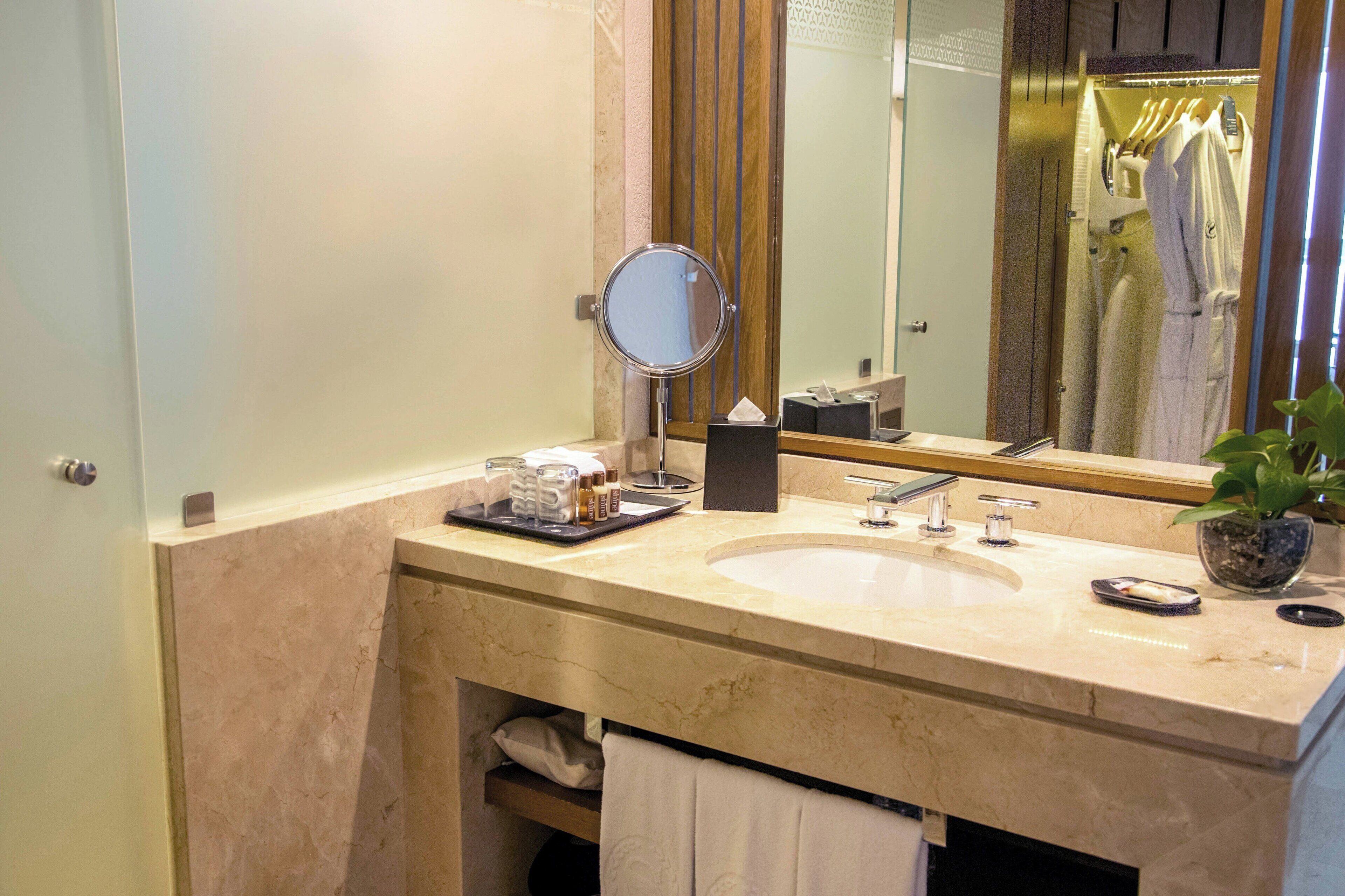 A bathroom with a marble sink, a round mirror, a towel rack, and a potted plant.