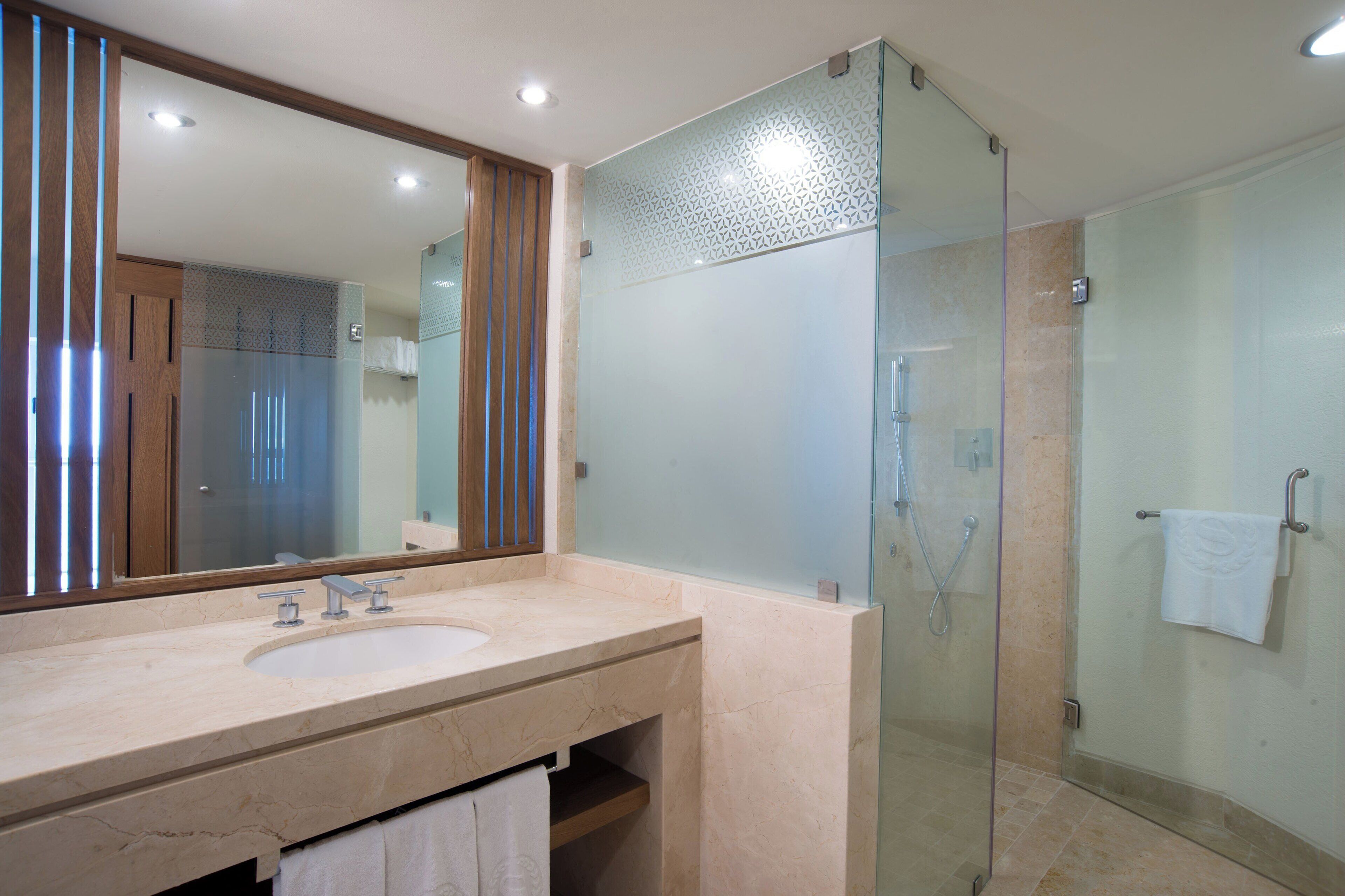 A modern bathroom with a glass-enclosed shower, a large mirror, and a marble sink.