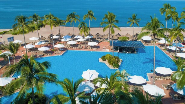 A resort pool with palm trees, umbrellas, and a beach view. - Sheraton Buganvilias Puerto Vallarta  (Puerto Vallarta)