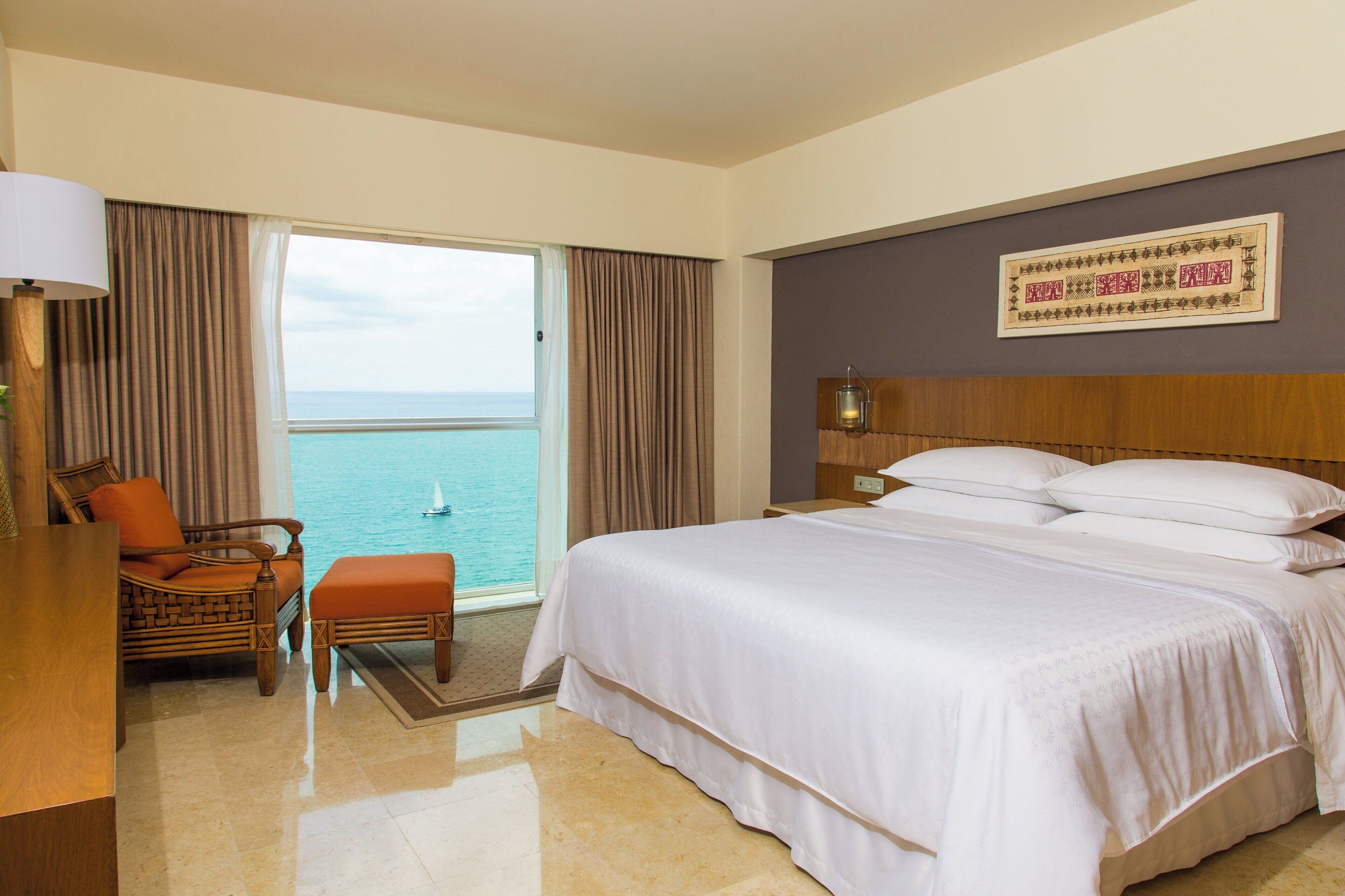 A hotel room with a large bed, a chair, a desk, and a view of the sea.