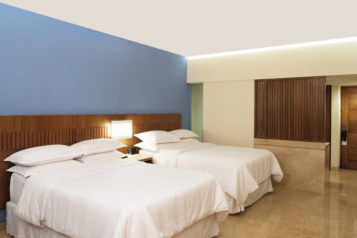 Ein Hotelzimmer mit zwei Betten, einem Holzkopfteil, einem Nachttisch mit Lampe und einer Holztür.