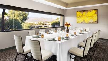 A conference room with a long table set for a meeting, chairs around the table, a window with a view of trees and mountains, and a yellow abstract painting on the wall.