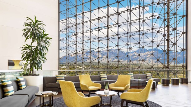 A modern lounge with a large window, a sofa, yellow chairs, and a potted plant. - Hilton Tucson East (Tucson)