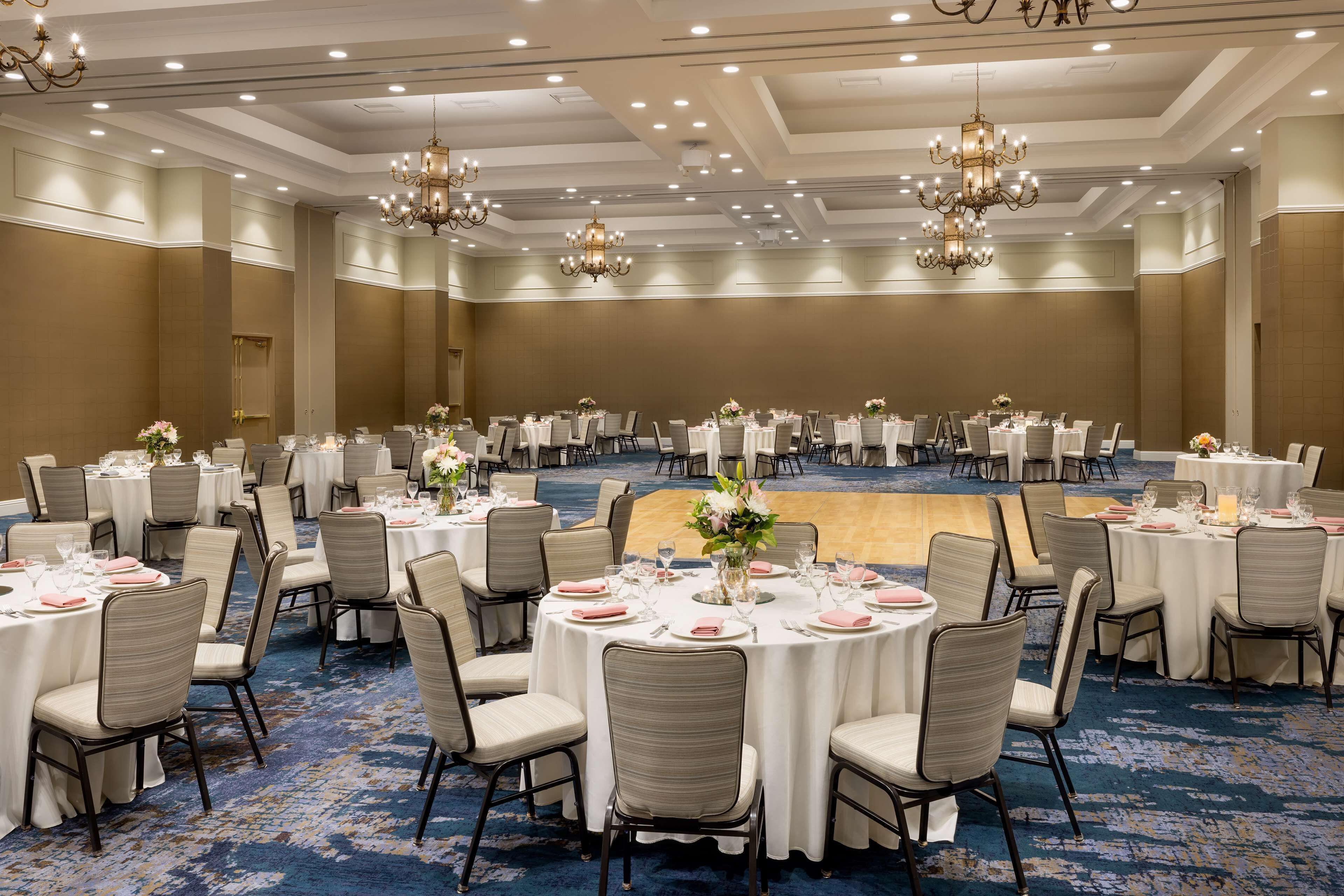 Un amplio salón de banquetes con mesas redondas dispuestas para cenar, con candelabros y piso alfombrado.