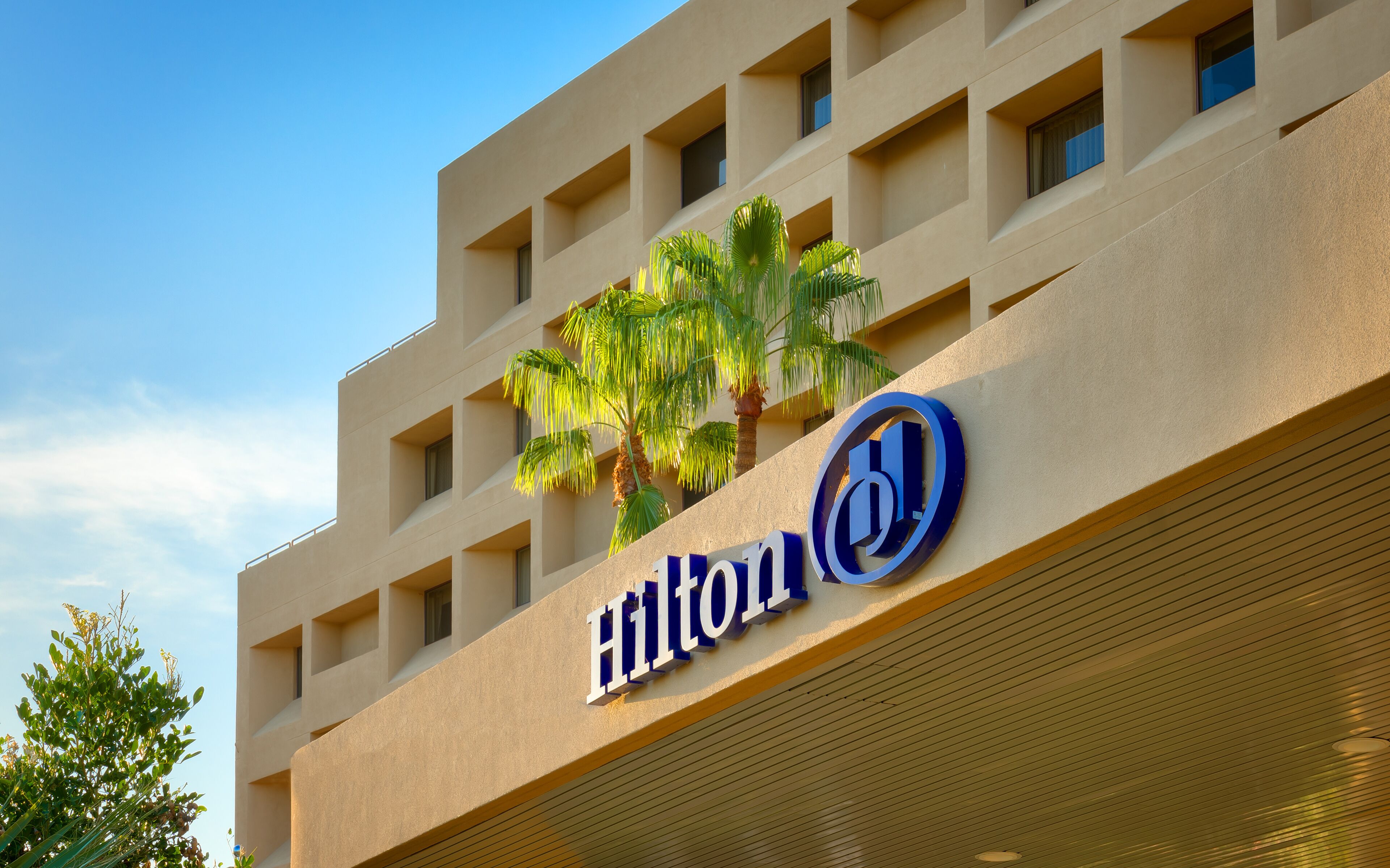 A building with a sign reading "Hilton" and a logo with a blue 'H'.