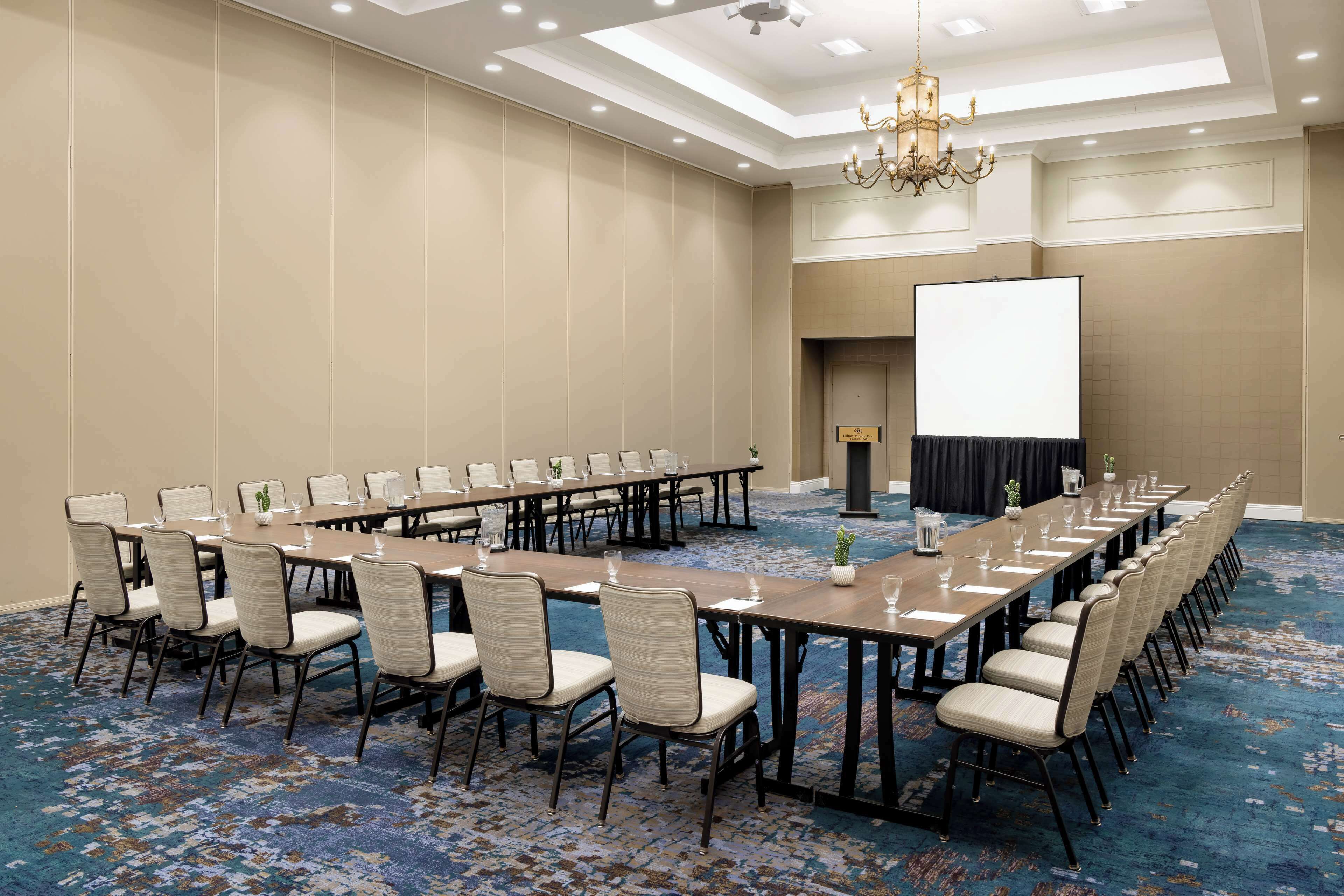 A conference room with a long table, chairs, a projector screen, and a chandelier.