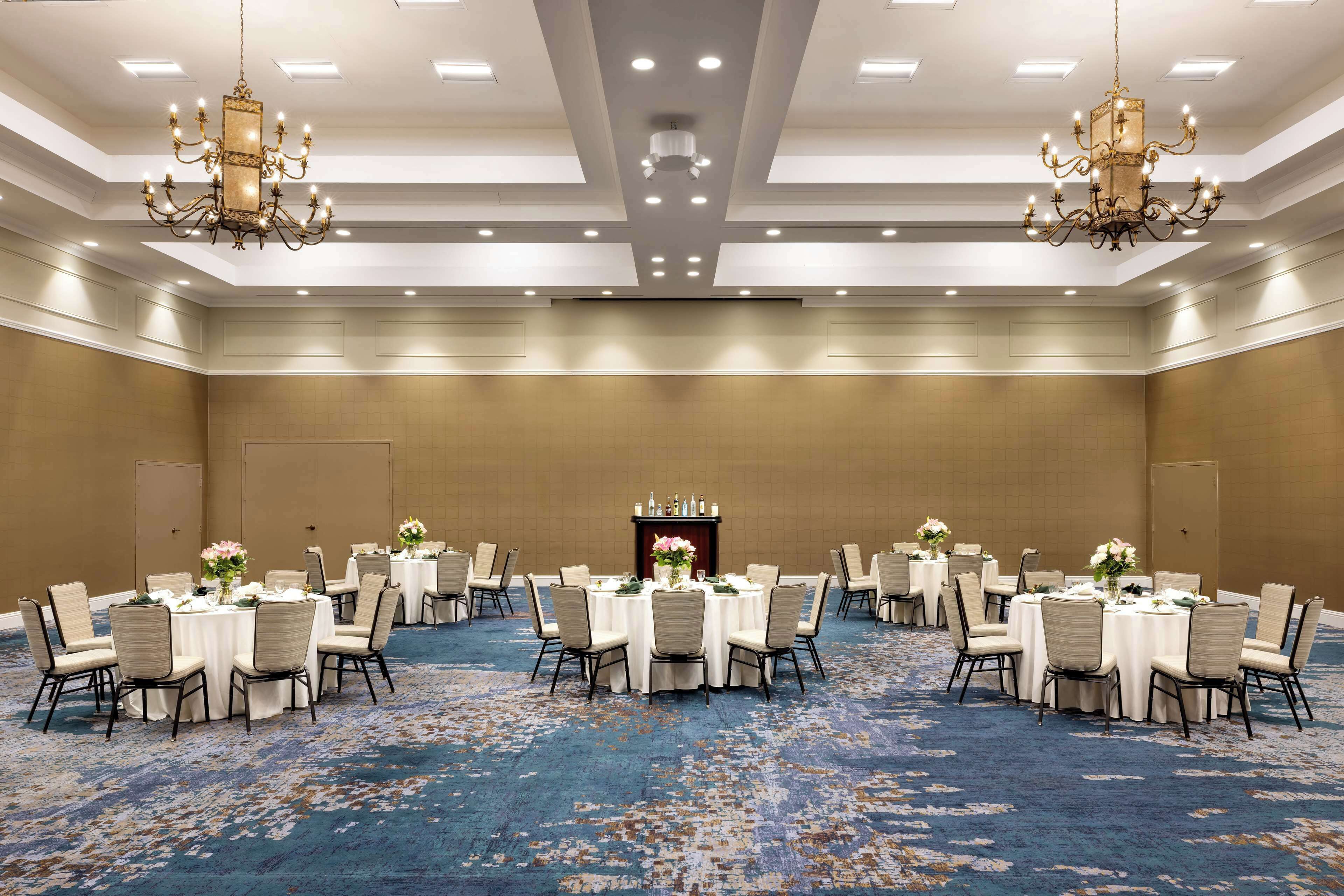 Un amplio salón de conferencias con varias mesas redondas, cada una con sillas y centros de mesa florales.