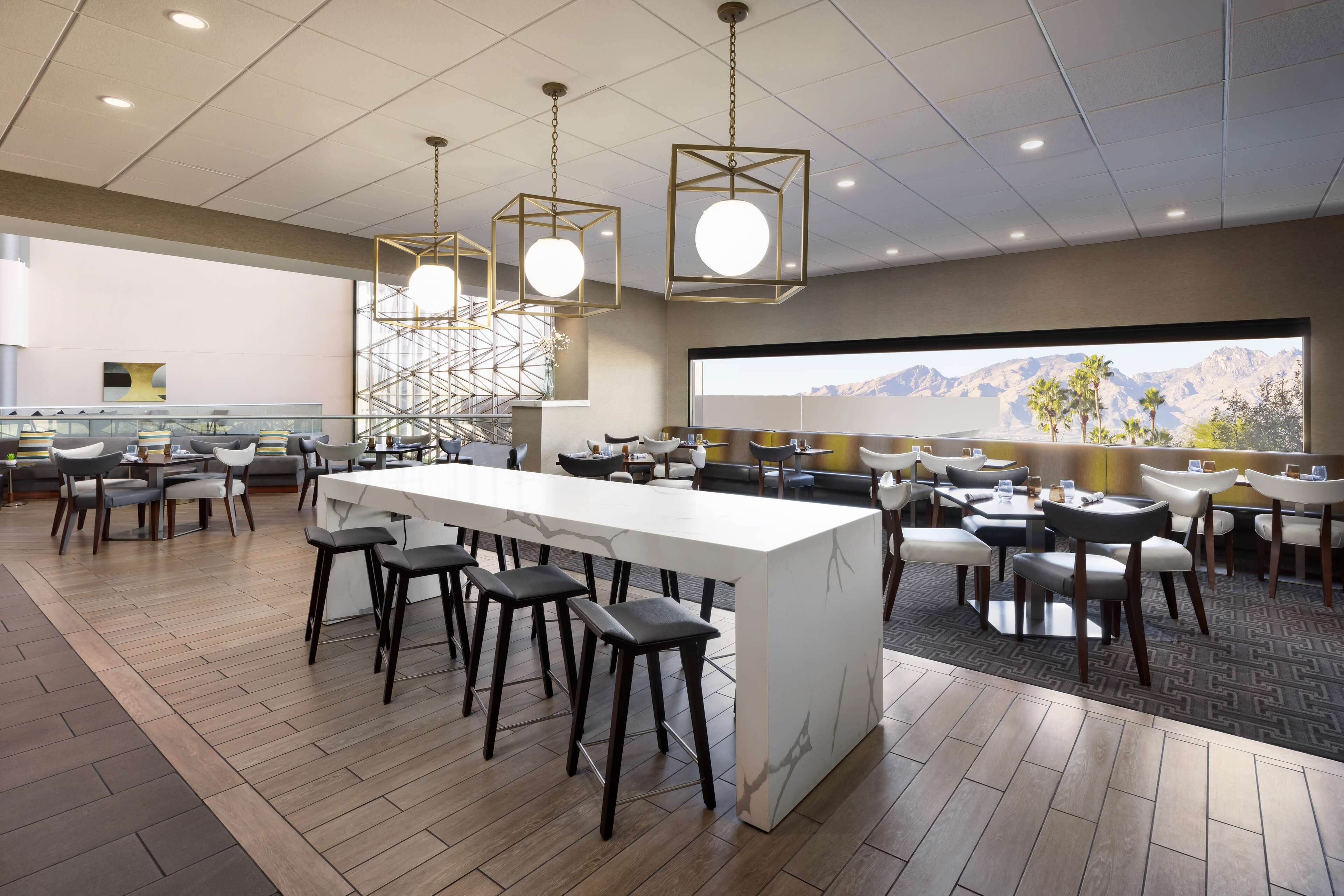 A modern restaurant with a central bar, multiple seating areas, and a large window offering a mountain view.