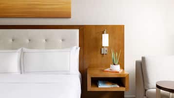 A hotel room with a tufted headboard, a bedside table with a lamp, a potted plant, and a chair.