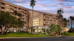 A large, modern hotel with a glass facade, multiple floors, and a well-maintained lawn with palm trees. - Hilton Tucson East (Tucson)