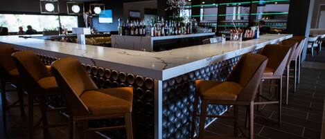 A bar area with a marble counter, cushioned bar stools, and a variety of bottles and glasses.