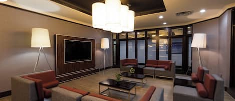 A modern lounge area with a flat-screen TV, comfortable seating, and large windows.