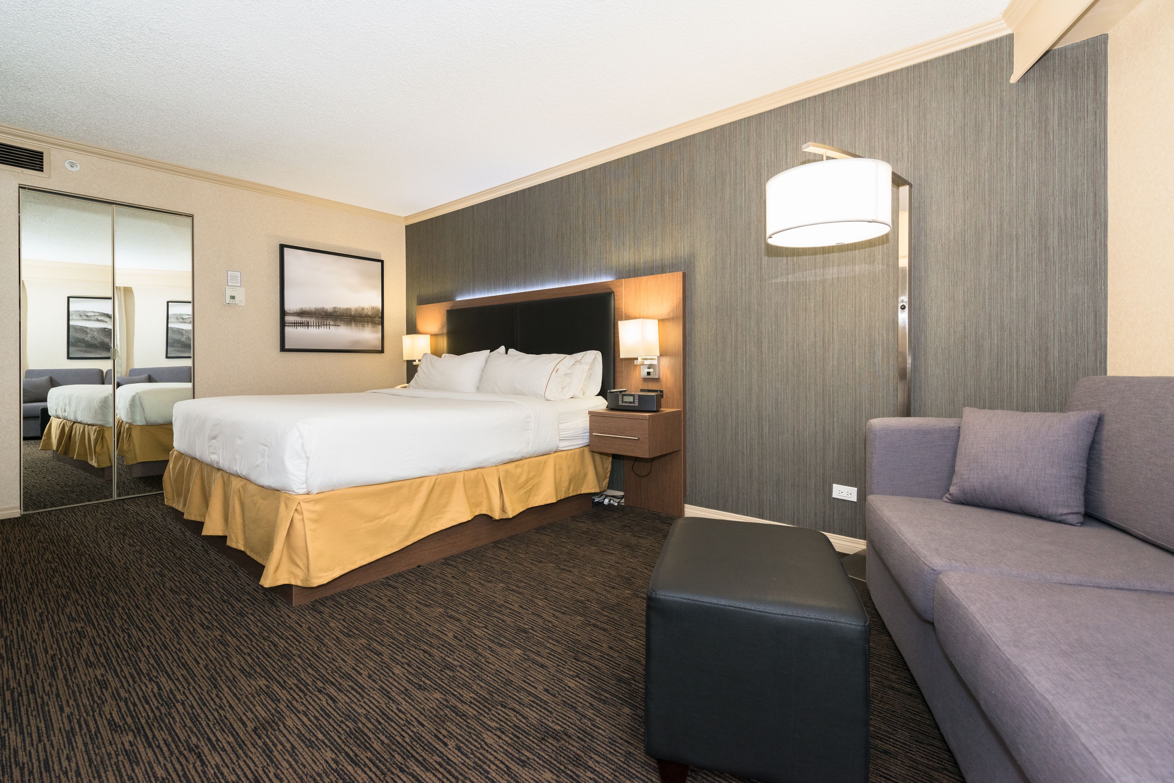 A hotel room with a large bed, a sofa, a desk, and a mirror.