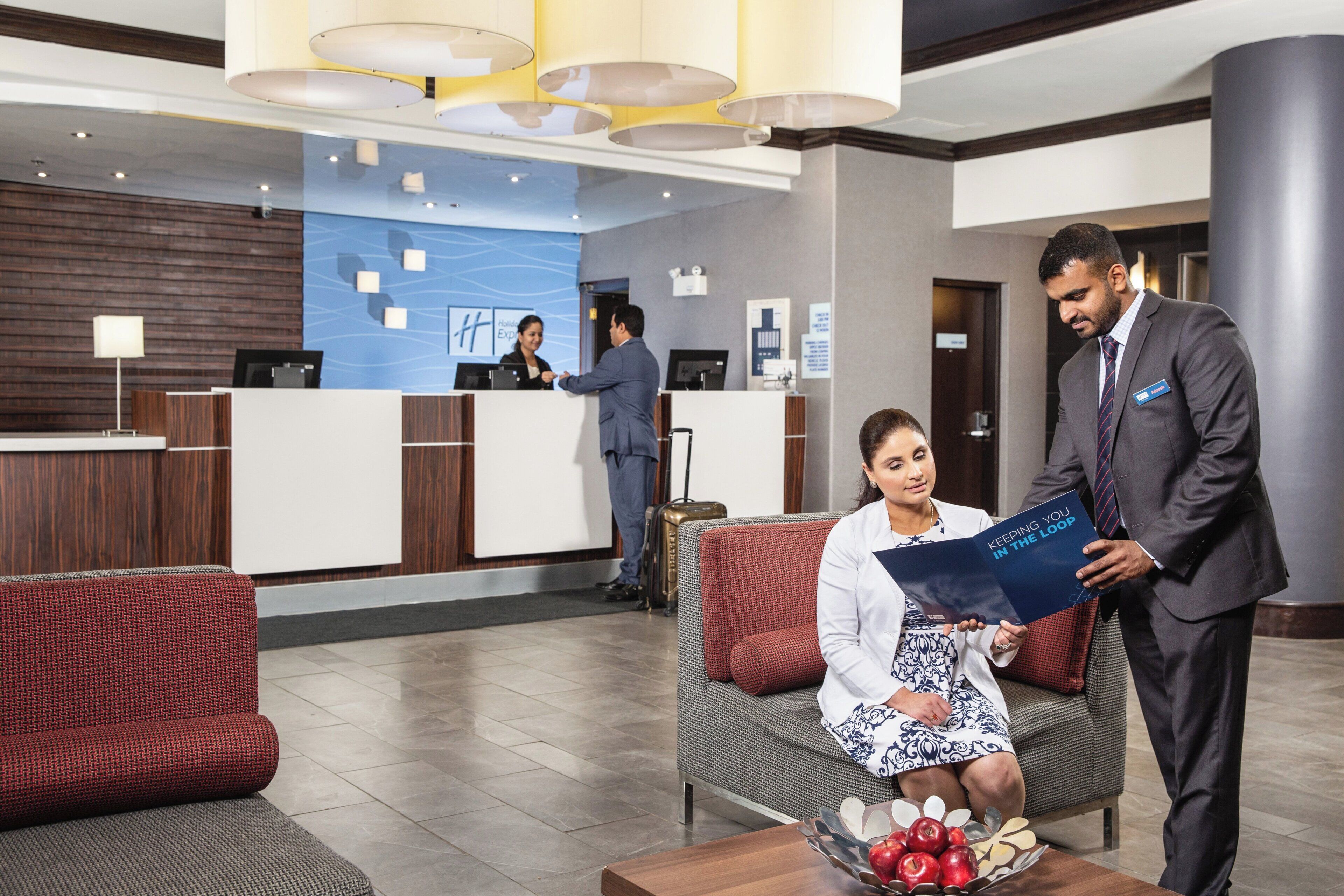A hotel reception area with a reception desk, a seating area with a sofa, and a coffee table with apples.