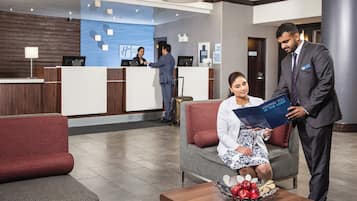 A hotel reception area with a reception desk, a seating area with a sofa, and a coffee table with apples.