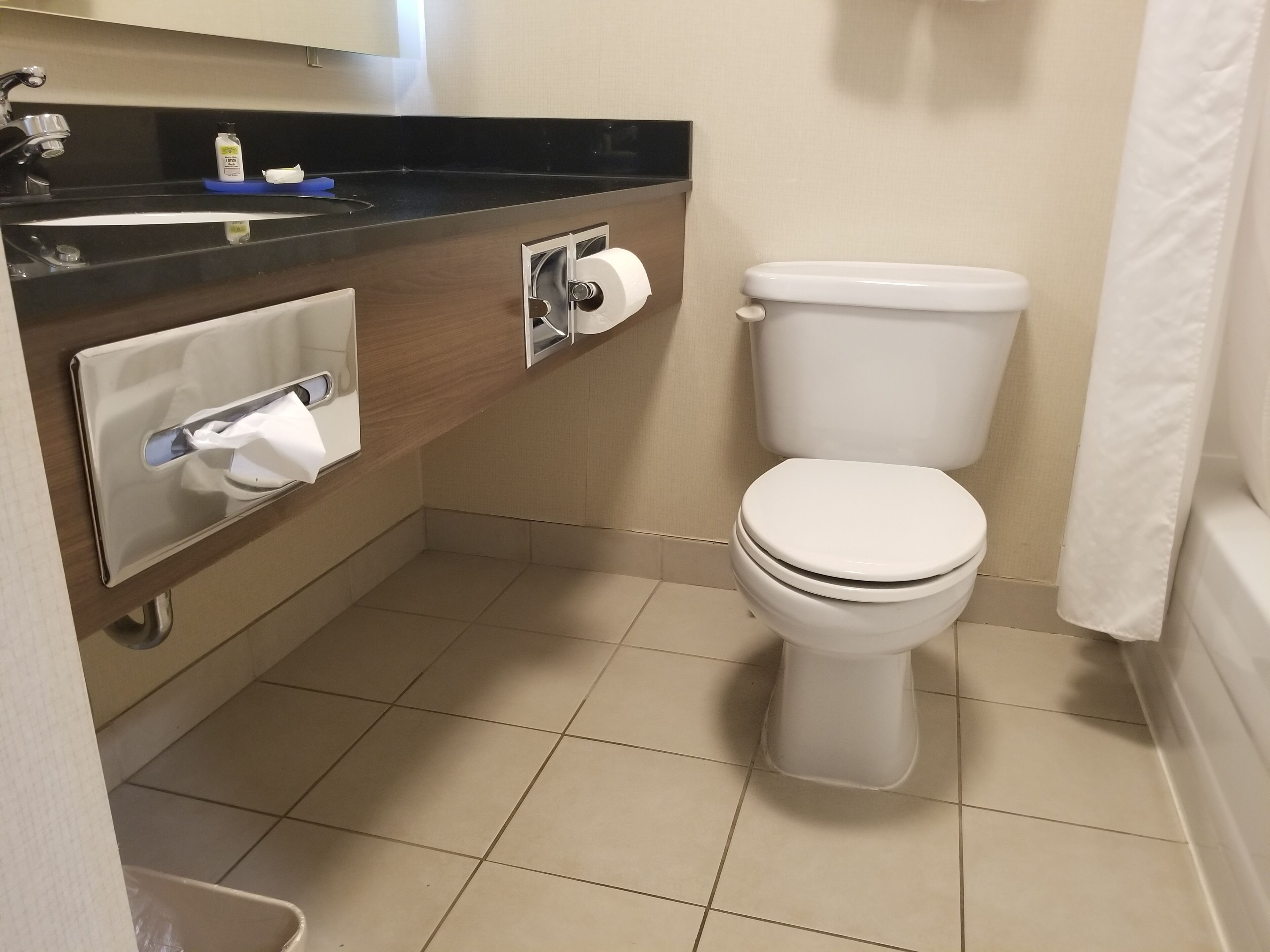 A bathroom with a toilet, a sink with a soap dispenser, and a paper towel dispenser.