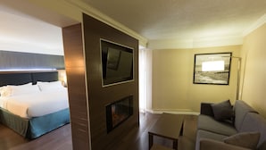 Habitación de hotel con cama, televisión montada en una pared de madera, chimenea, sofá y un cuadro en la pared.