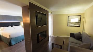 Habitación de hotel con cama, televisor de pantalla plana en pared de madera, chimenea, sofá y un cuadro enmarcado.