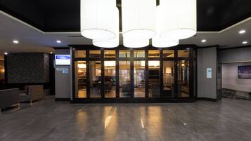 Een hotel lobby met een modern design, met een receptiebalie, een zithoek en een glazen deur die naar de kamers leidt.