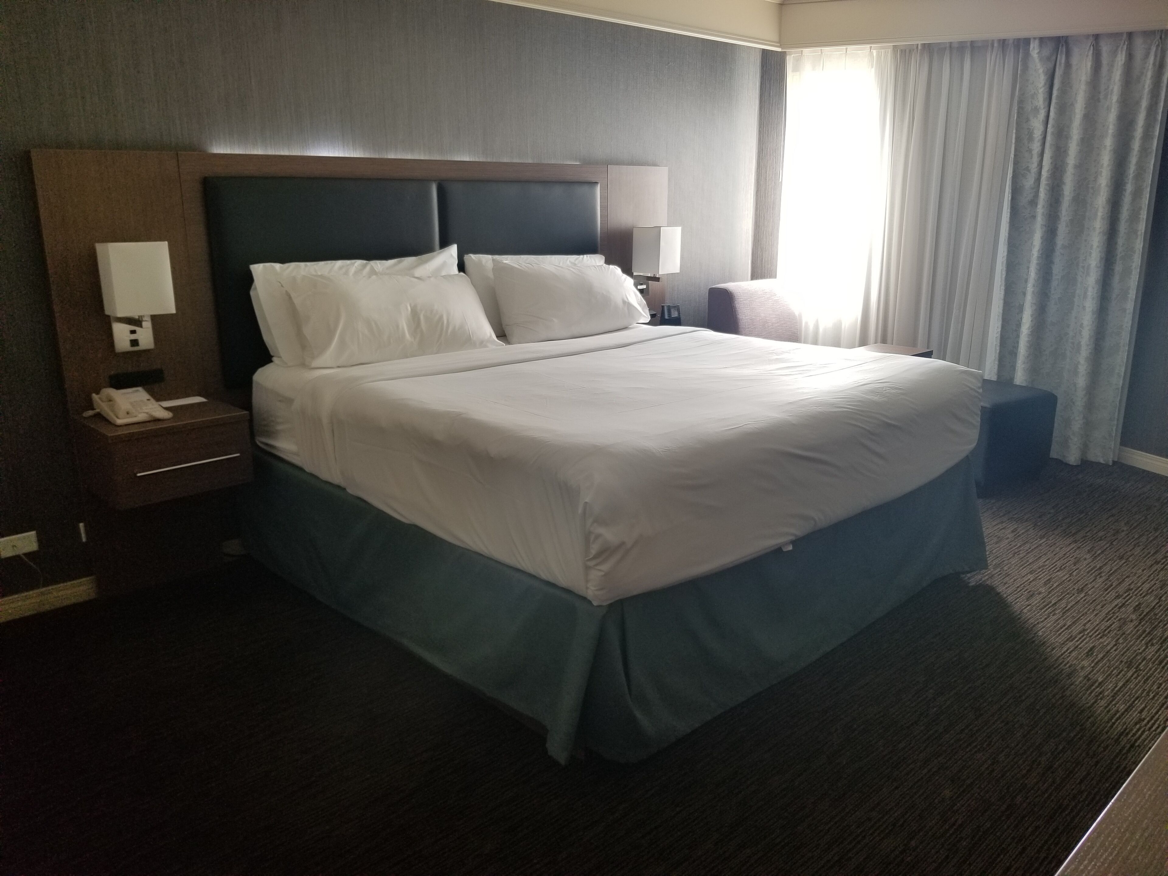 A hotel room with a large bed, a nightstand with a phone, a lamp, and a small table.