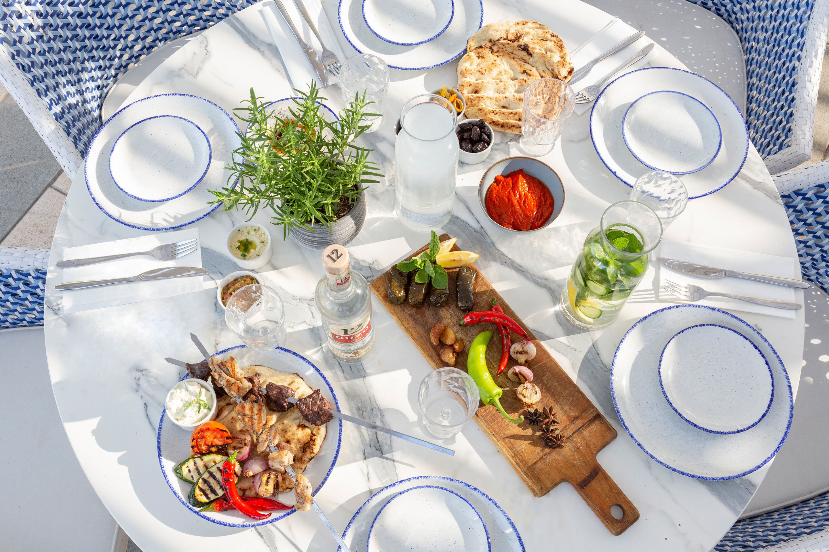 Een ronde eettafel met een witte marmeren blad, blauw randje borden en netjes geranguleerd bestek.