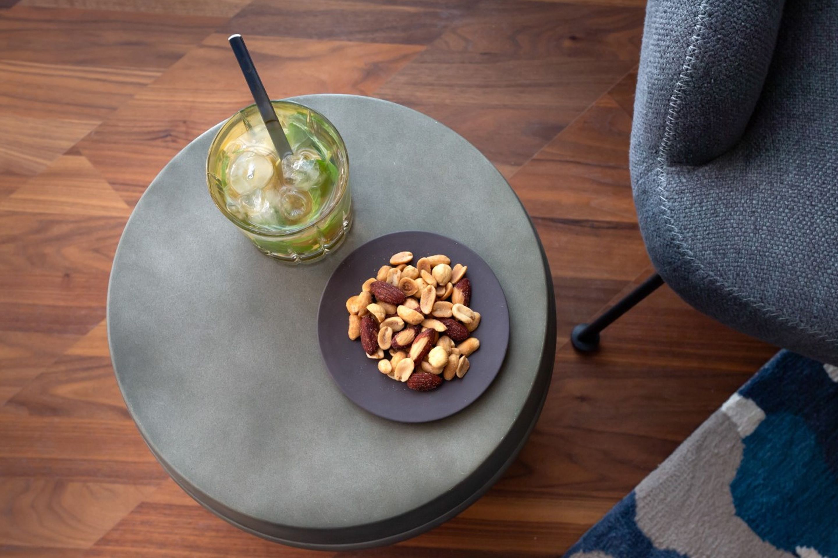 Una mesa redonda con un vaso de bebida helada y un plato de nueces.