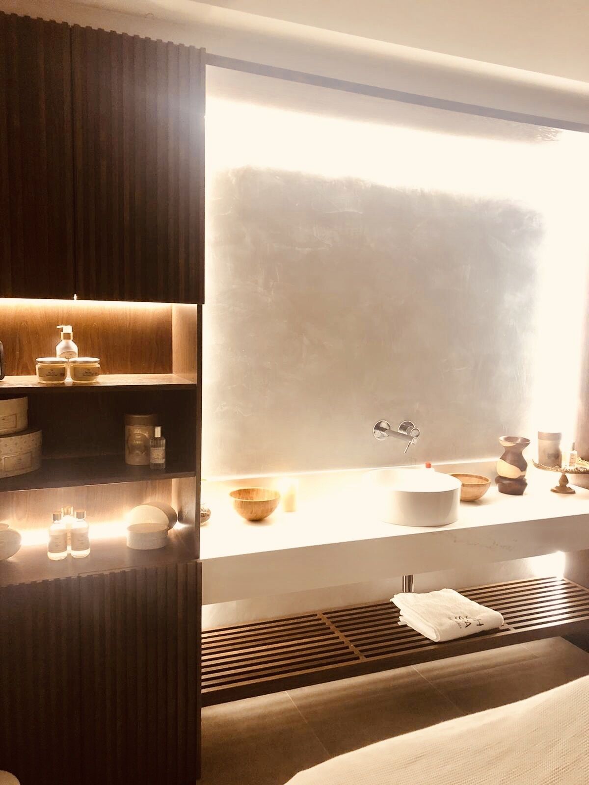 Un baño moderno con un ventanal amplio, un lavamanos con grifo y repisas con artículos de aseo.