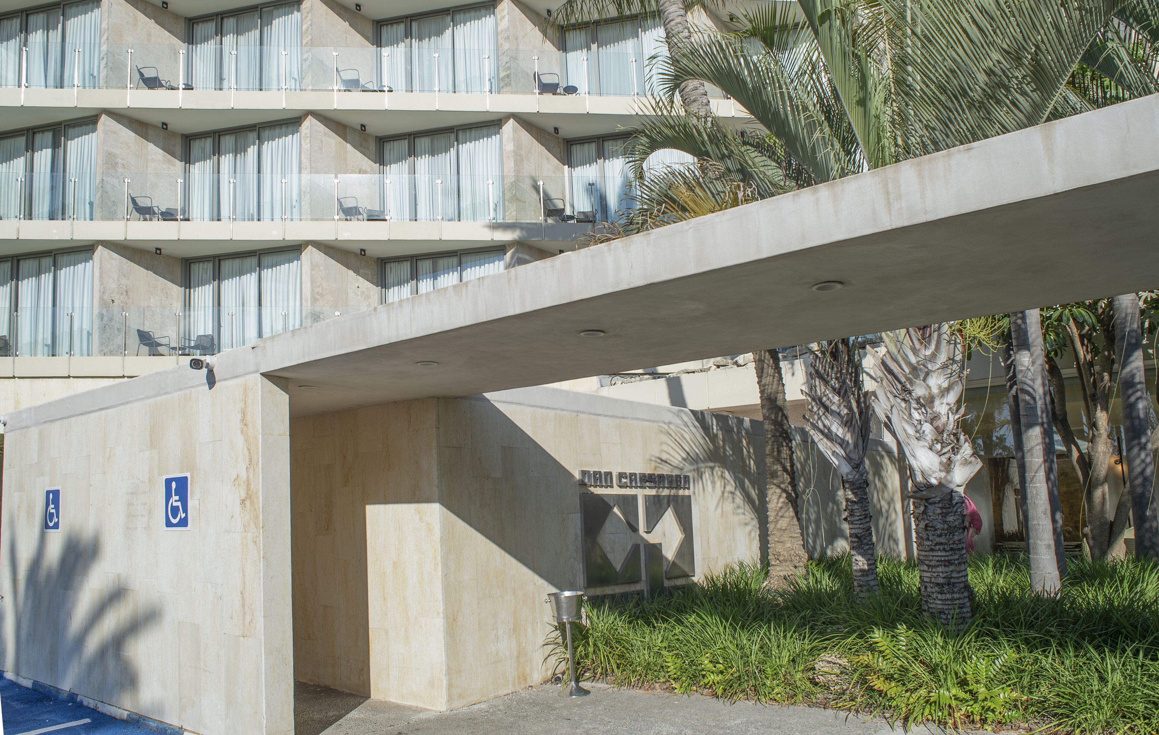 Edifici modern amb façana de formigó, una rampa que condueix a un nivell inferior i un senyal que indica una zona d'aparcament per persones amb discapacitat.