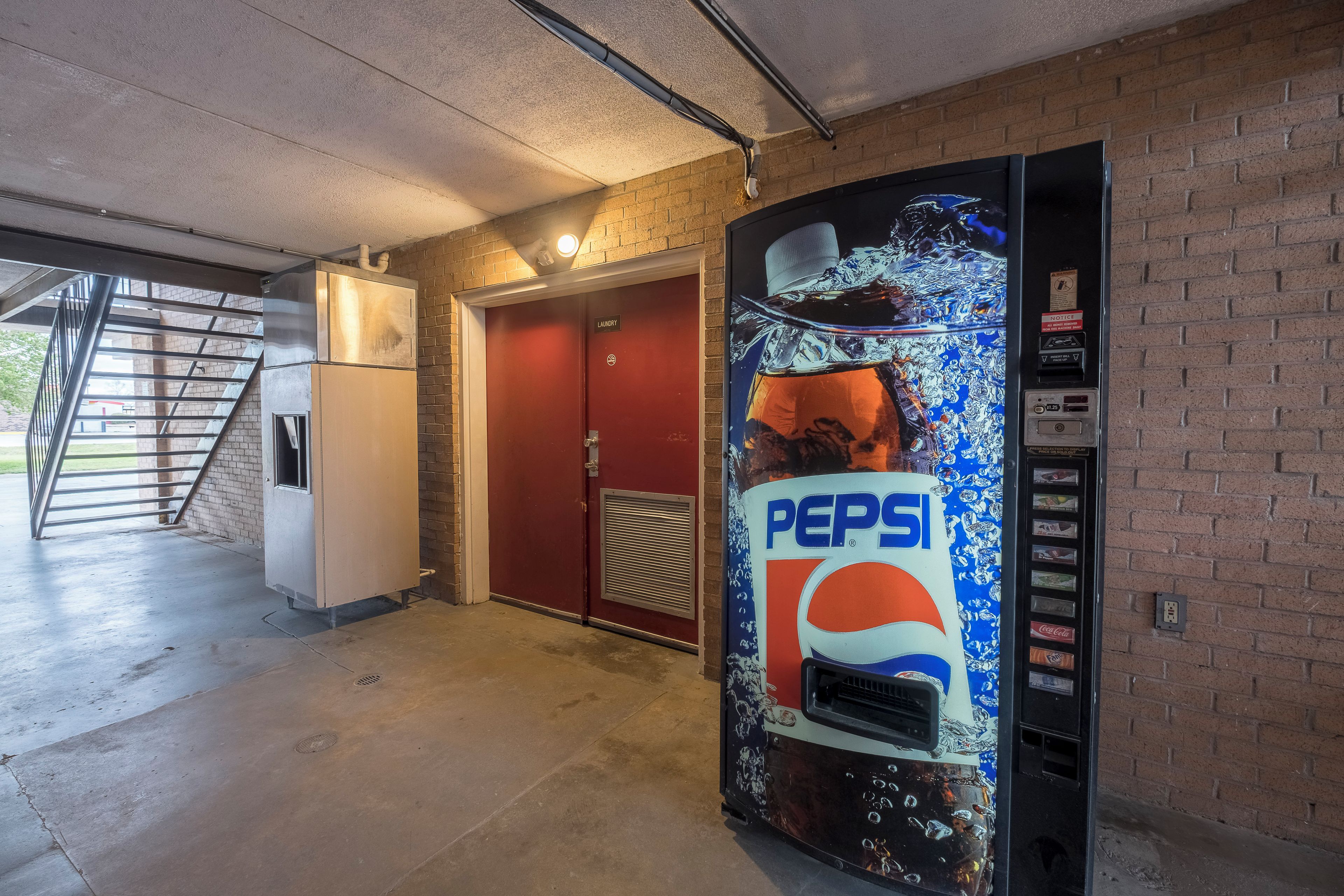 A vending machine with a Pepsi logo, a red door, and a white appliance in a hallway.