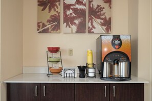 Un coin café équipé d’une machine à café, d’une pile de gobelets jetables et d’un présentoir à trois niveaux avec des bols.